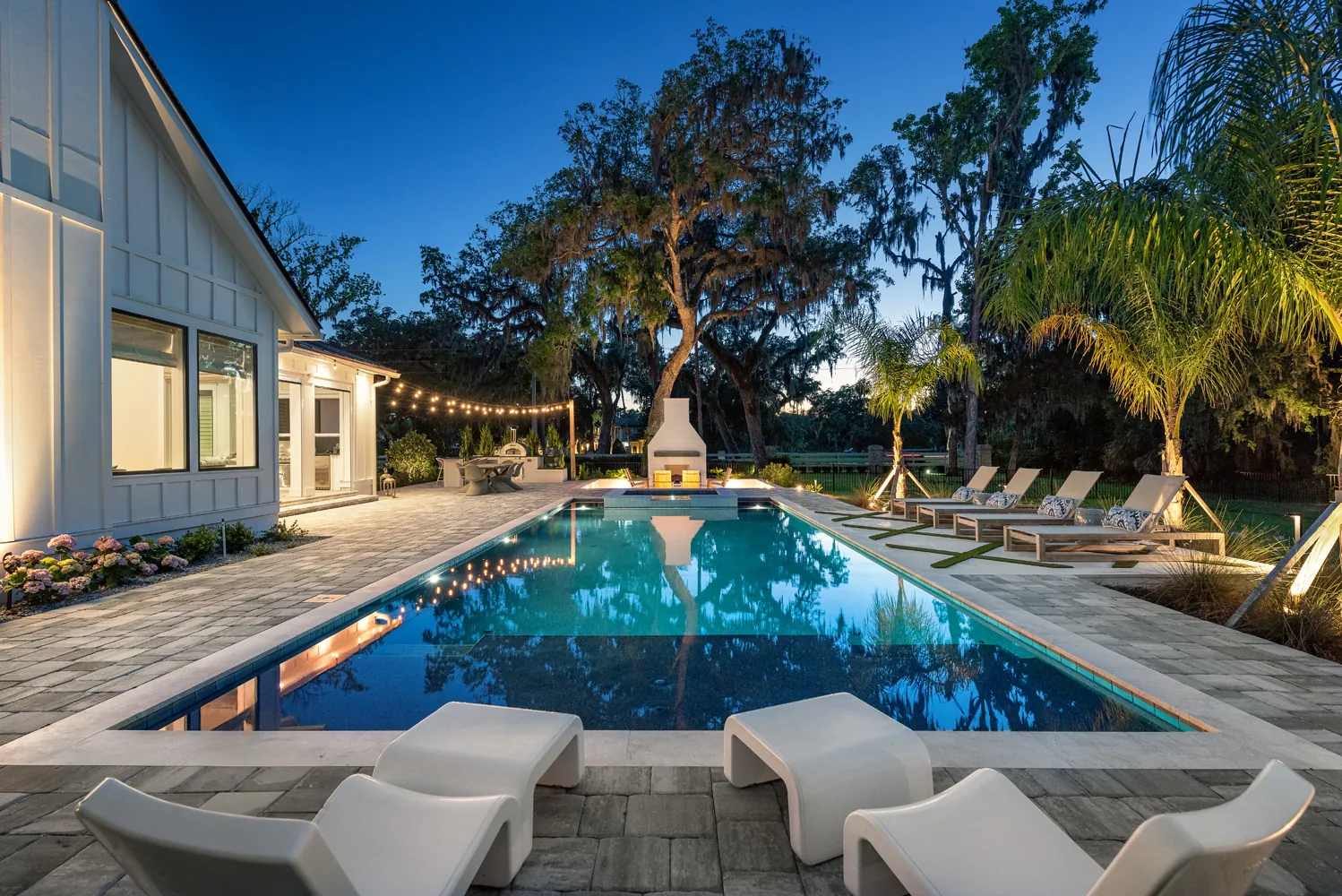 Luxury custom backyard pool with modern paver decking, outdoor fireplace, and string lights by Clarkson Pools in Jacksonville, Florida.